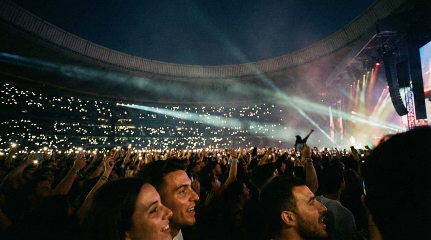 Multitud en un concierto de noche en un estadio, con miles de luces de celular en alto